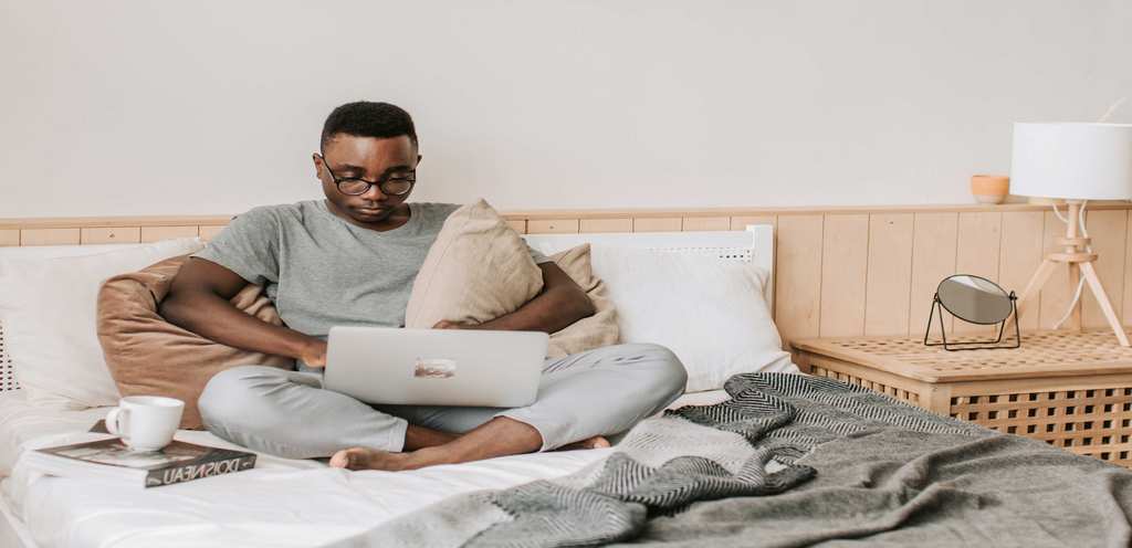 Ein Mann sitzt auf dem Bett mit einem Laptop auf dem Schoß.